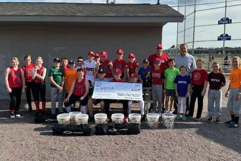 Youth baseball players and coaches with a donation check and new equipment at a ballfield