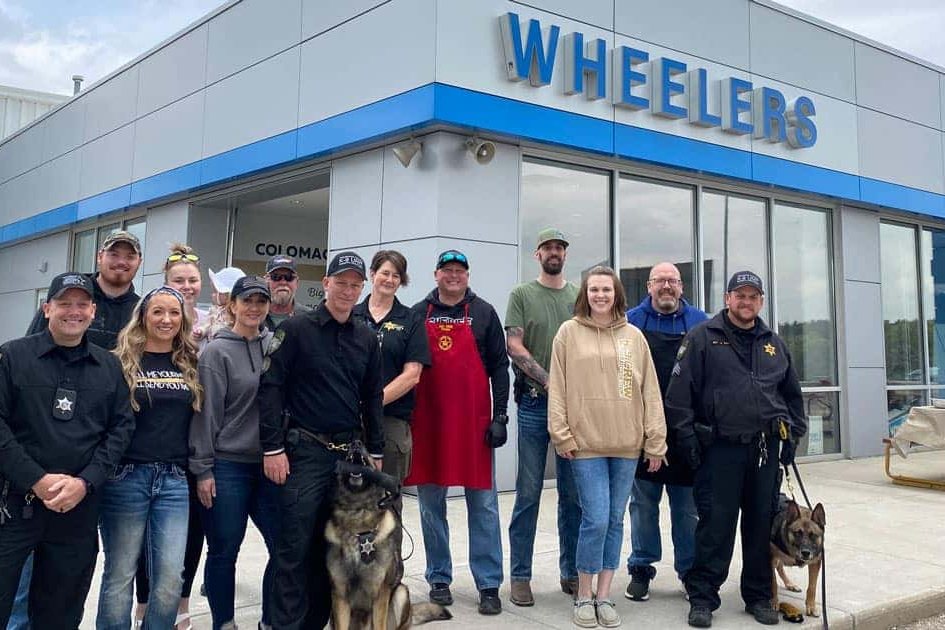 Wheelers team members and sheriff deputies with two K9 dogs outside Wheelers Chevrolet of Coloma