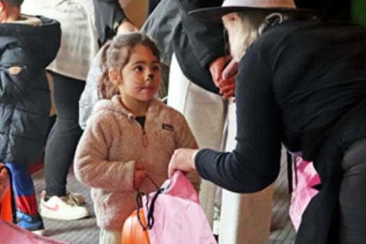 Child in face paint receiving a pink bag from a volunteer in a witch hat